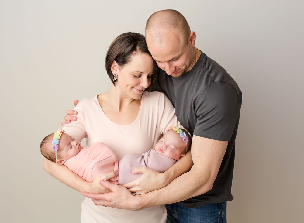 family photo of mom and dad holding newborn twin girls and gazing down at them
