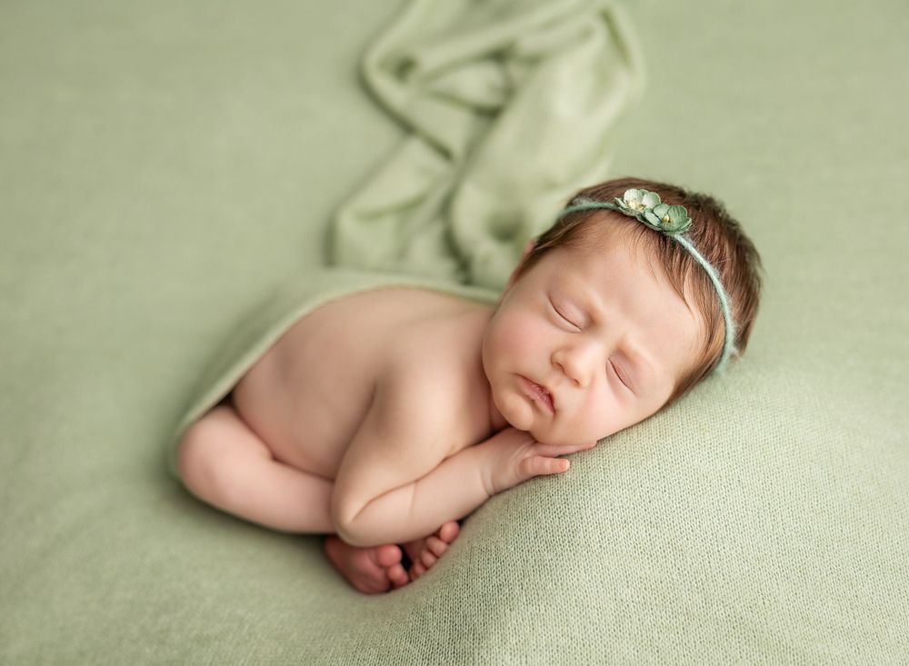 newborn sleeping baby on a green backdrop with a little headband on