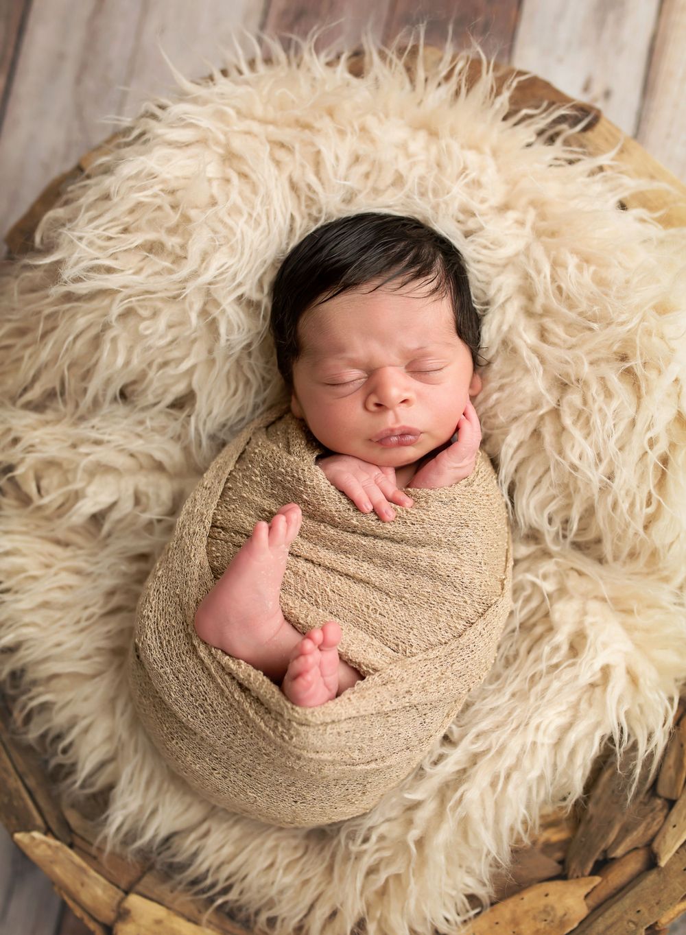 newborn boy with a lot of black hair sleeping in a wrap in a basket