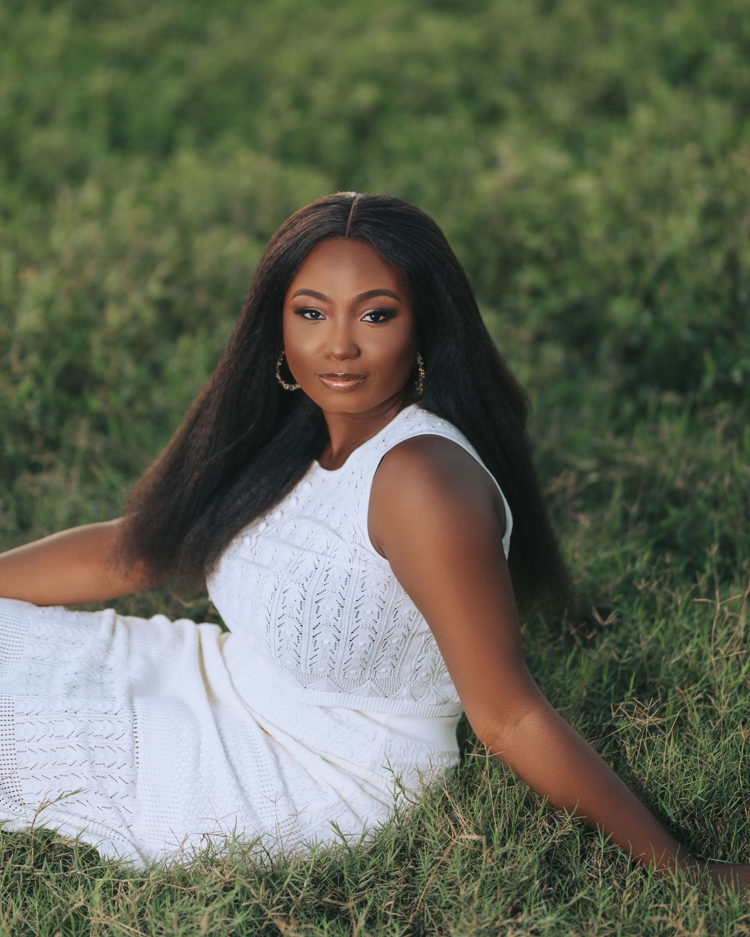 A woman in a white dress poses gracefully on grass during an outdoor photo session.