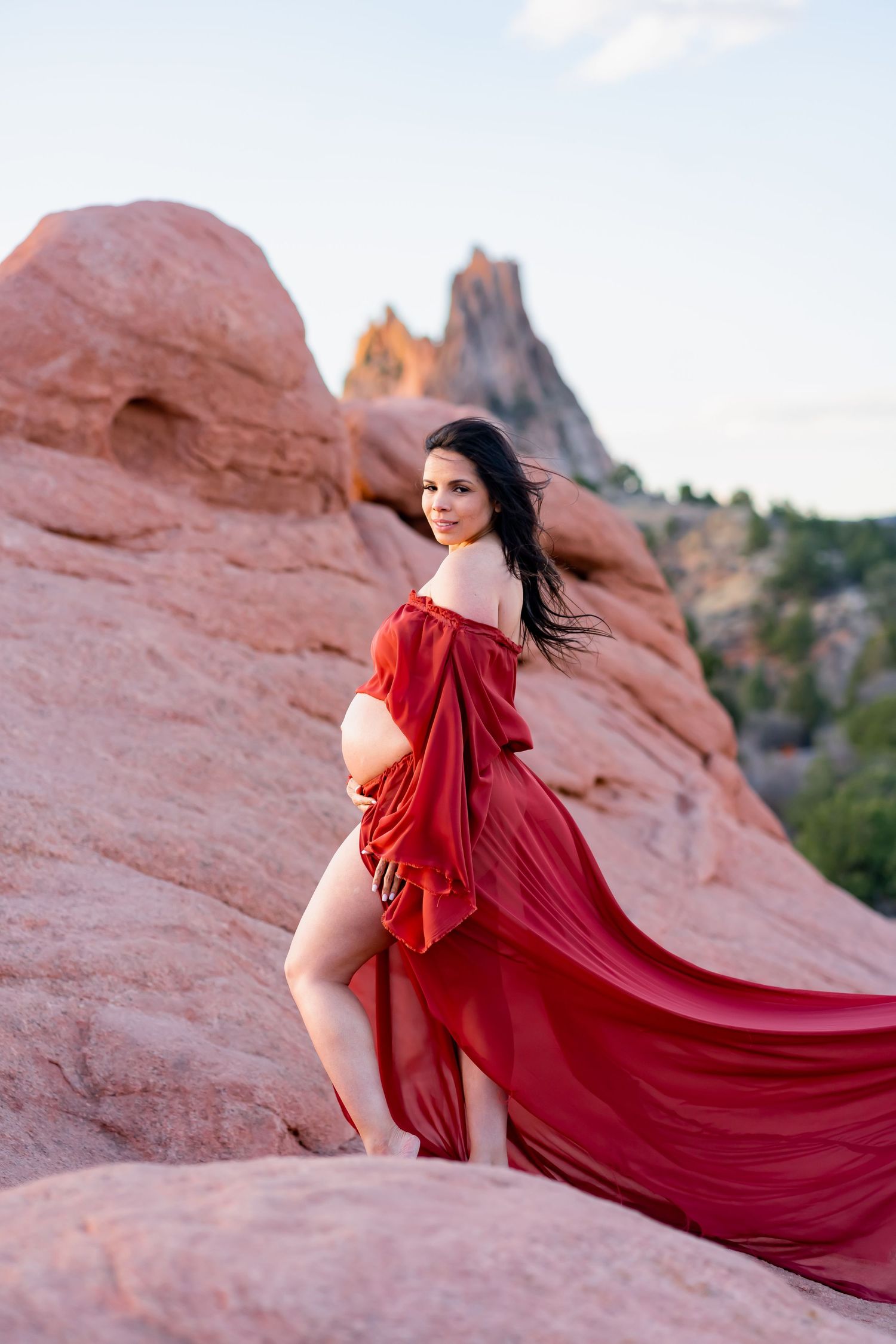 A flowing red gown contrasts beautifully against red rock formations in a desert landscape at sunset.