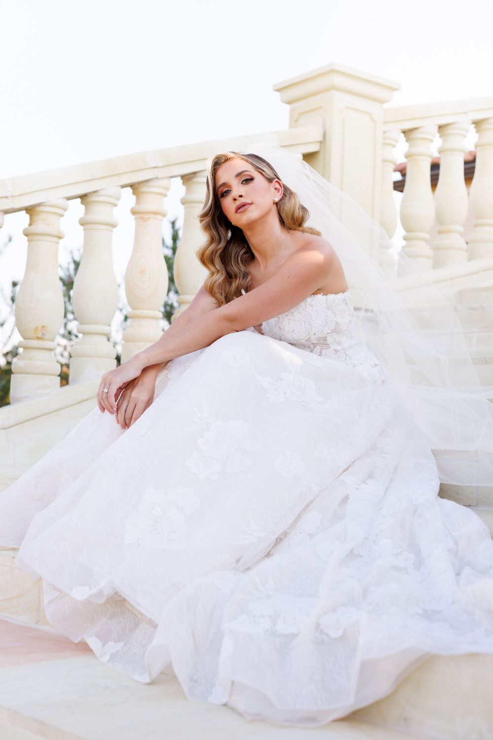 Elegant bridal poses on white stone balcony showcasing full wedding gown and veil in natural light.