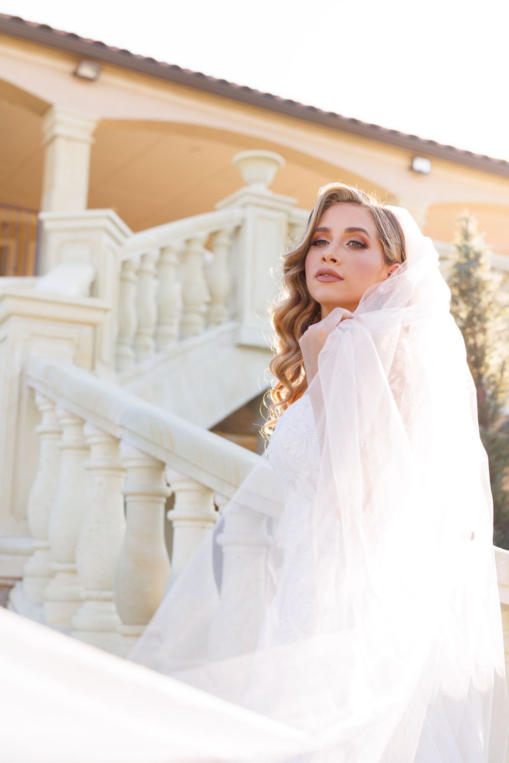 Romantic bridal portraits with soft lighting and flowing veil against Mediterranean-style architecture.