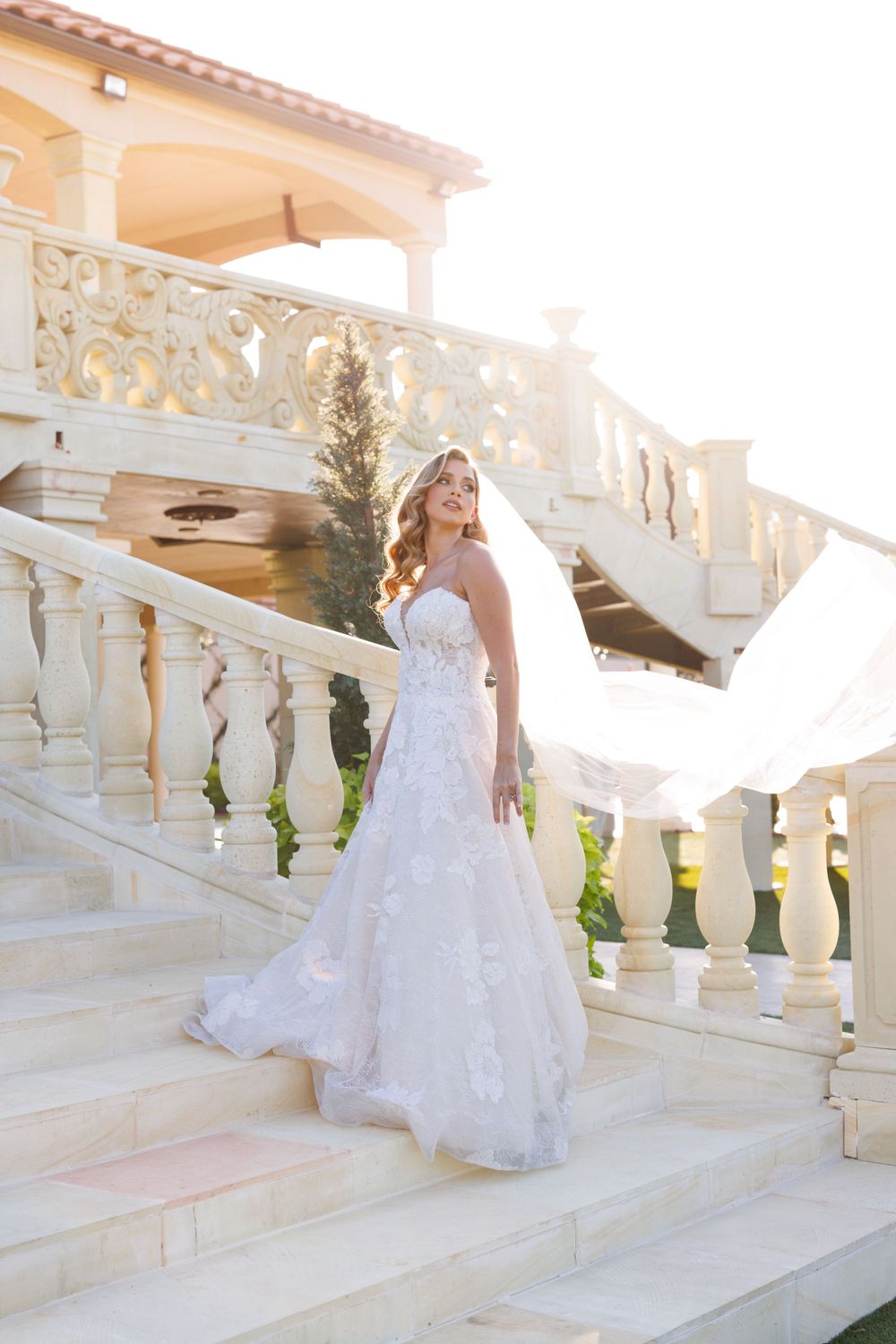 Wedding dress with long train cascading down ornate white stone steps in elegant outdoor setting.
