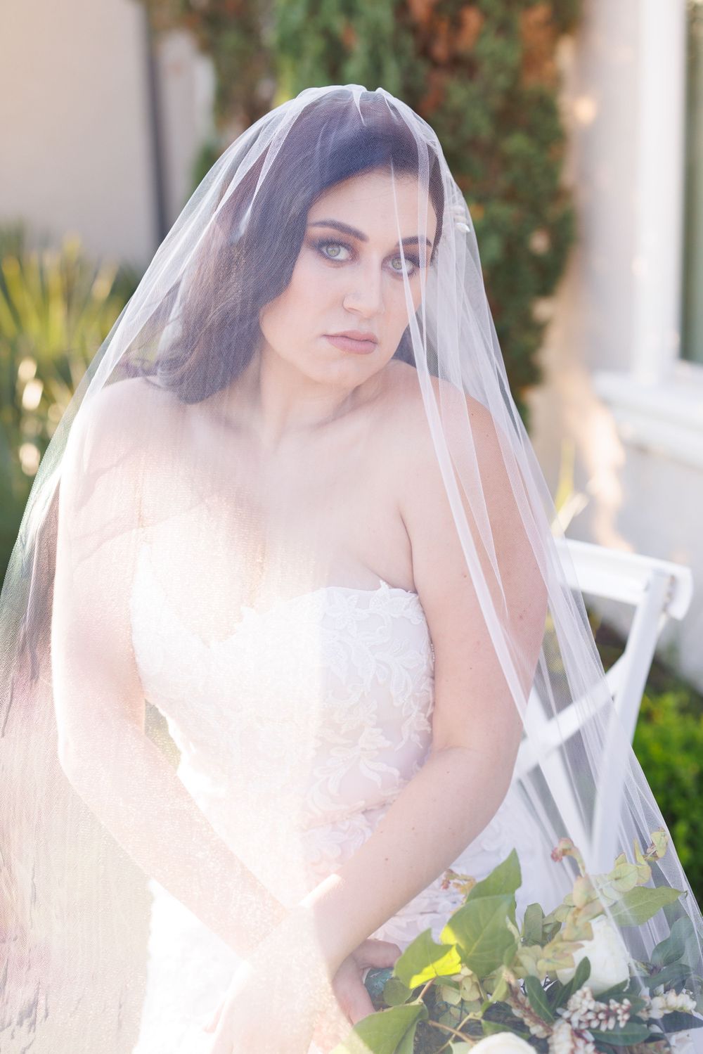 Soft sunlit bridal portraits with delicate veil and white floral bouquet against garden backdrop.