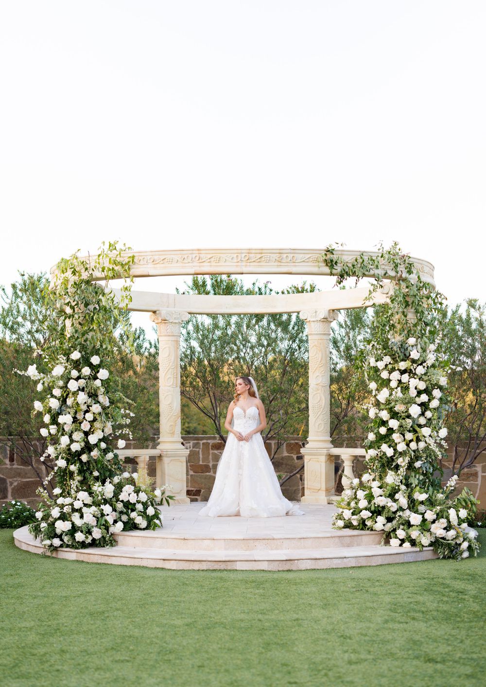 Wedding photography at an elegant stone pavilion decorated with white roses and greenery.