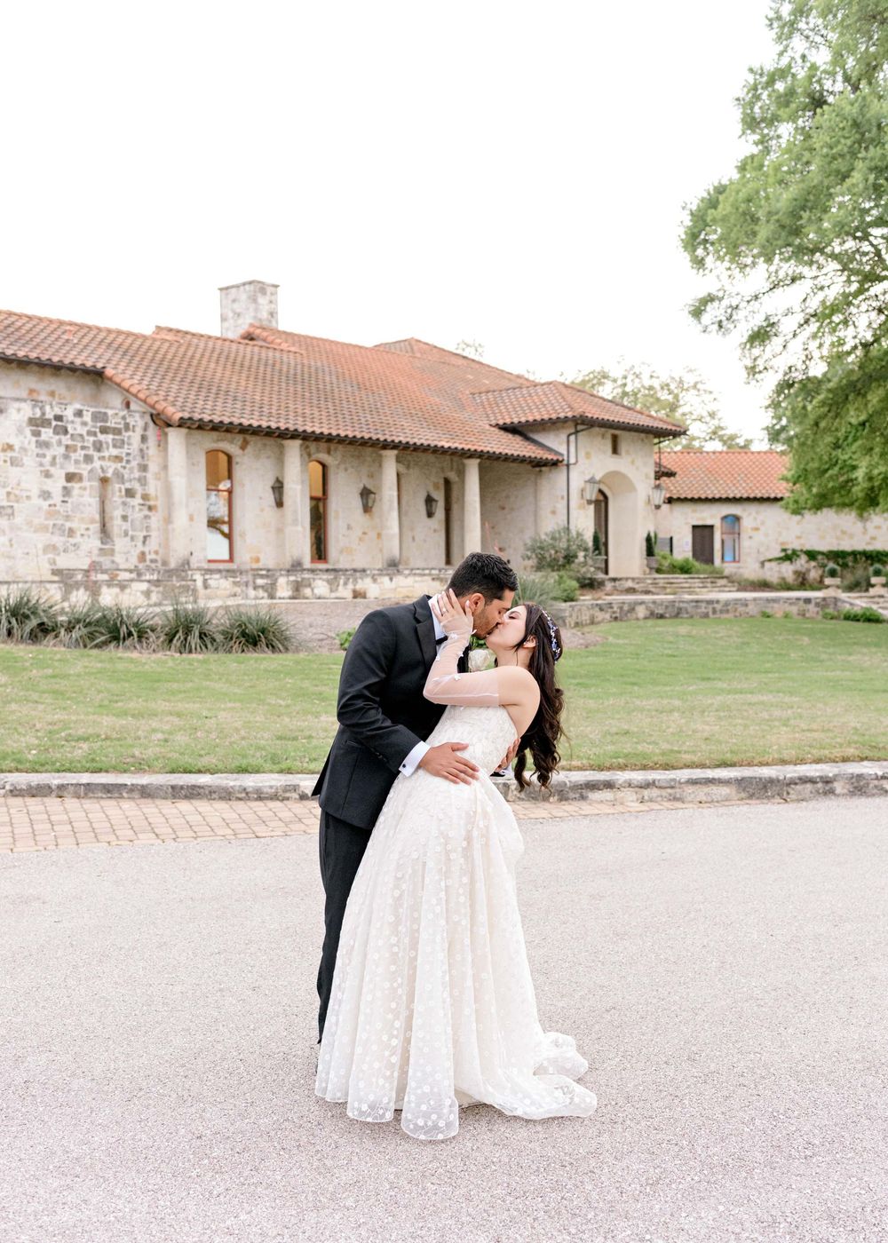 A wedding couple shares romantic kisses in different poses outside a Spanish-style building with terracotta roof.