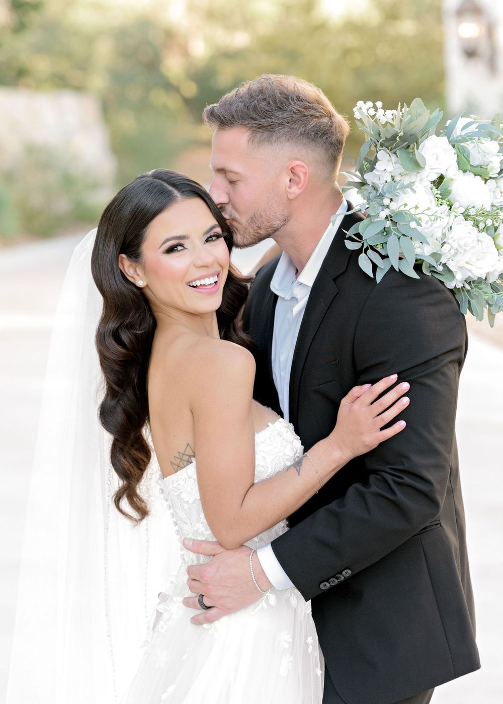 Newlywed couple shares romantic moments in outdoor wedding photos with white floral bouquet and elegant attire.