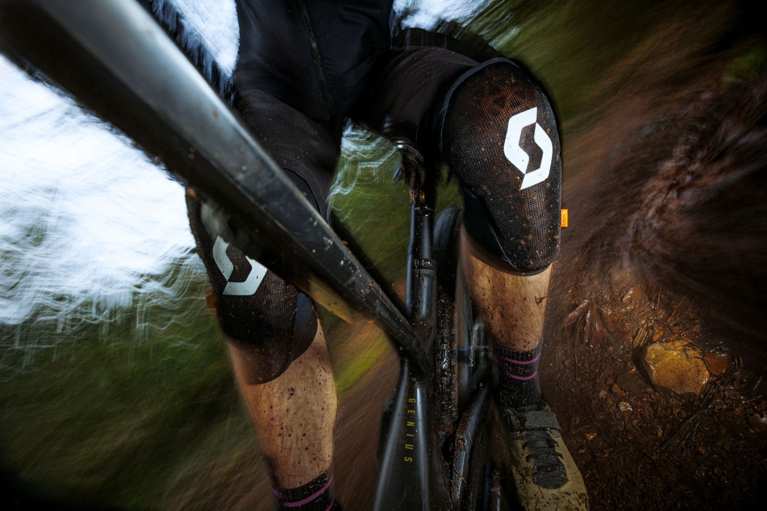 Close-up of Scott bike knee pads during trail ride through muddy terrain.