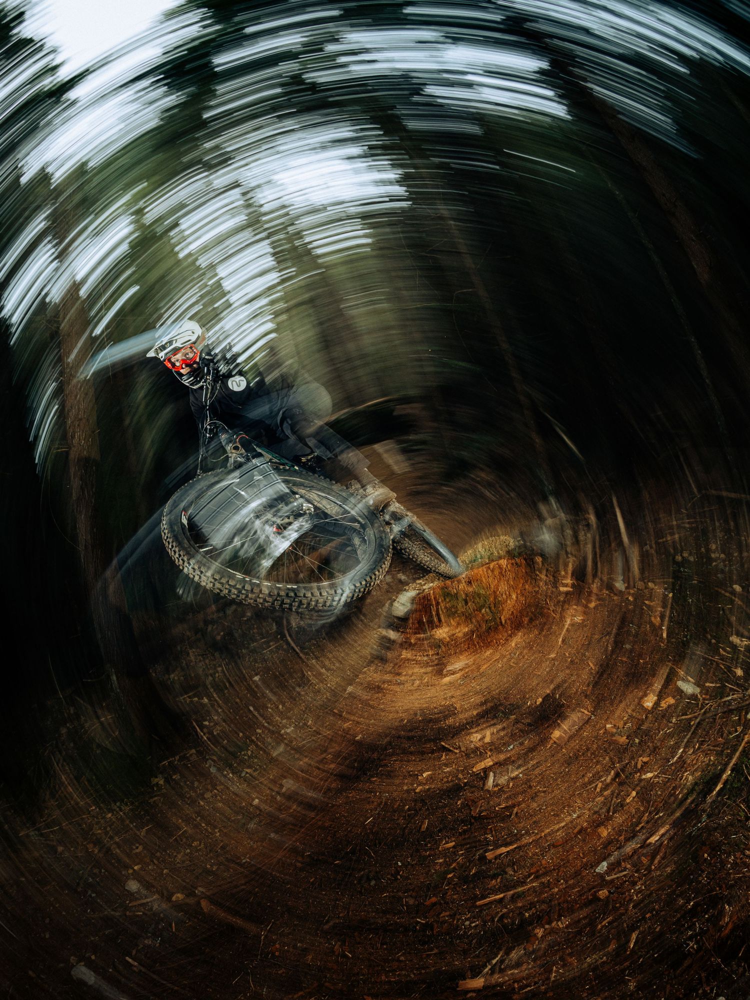An artistic motion-blur photo of a mountain biker racing through a curved dirt trail captured with circular swirl effect.