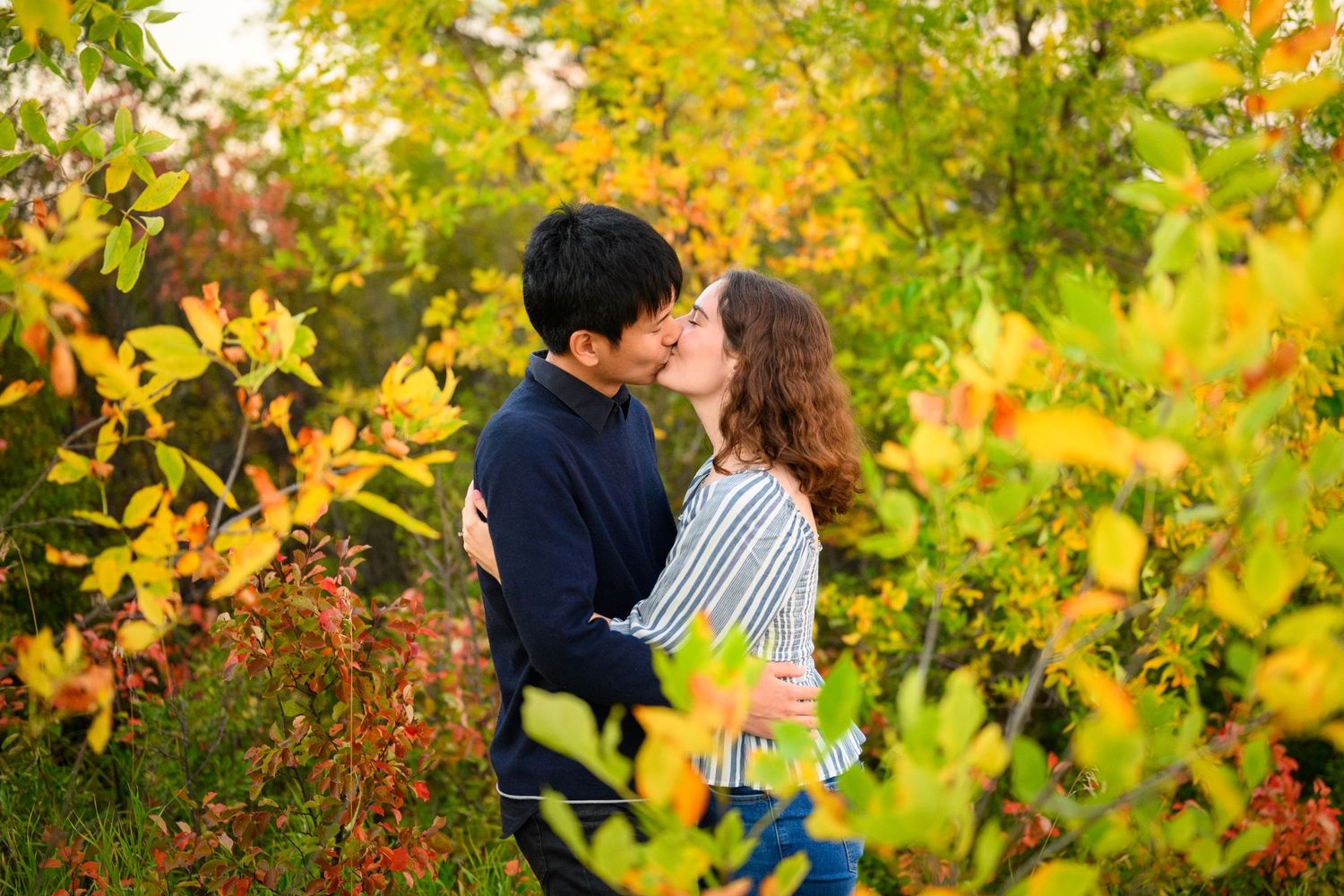 Romantic couple sharing an intimate moment among vibrant fall foliage in a natural outdoor setting.