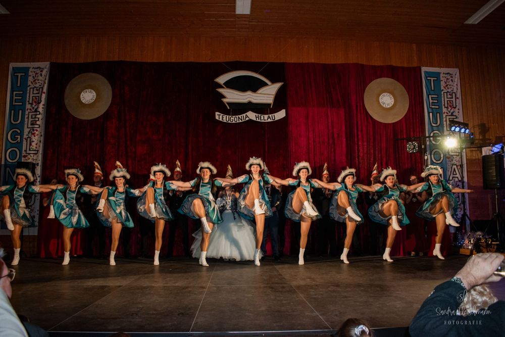 Dance performers in matching outfits create a synchronized line formation on a dimly lit stage.