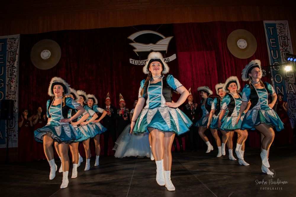 Synchronized dance performance with dancers in blue and white costumes on stage under dramatic lighting.