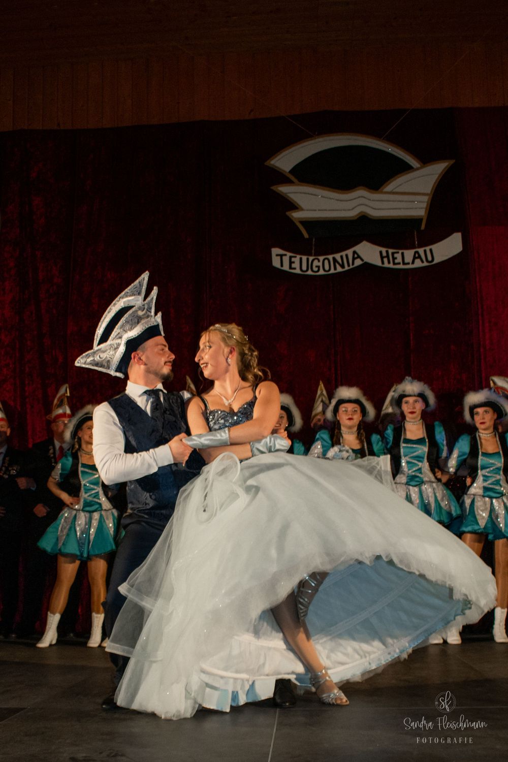 A wedding couple performs a romantic dip dance move in front of performers wearing matching turquoise outfits.