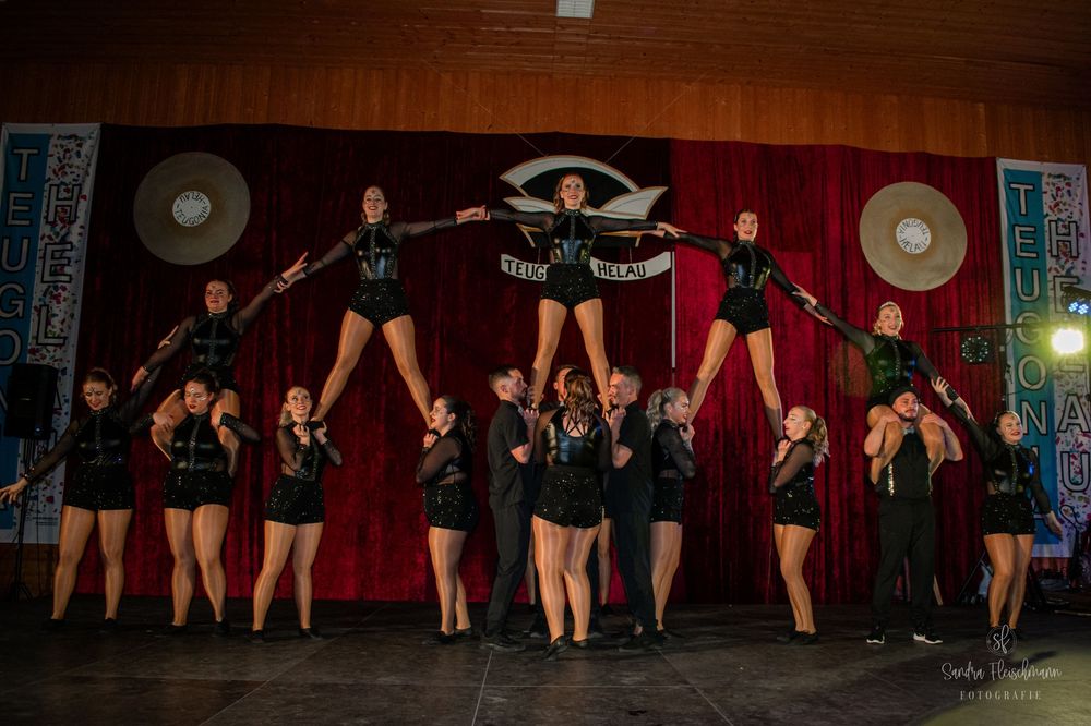 Dance performers in black outfits strike dynamic poses on stage in front of a red curtain during a show.