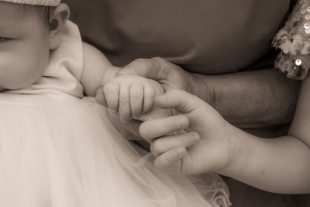 A tender sepia-toned photo of a newborn baby grasping an adult's finger, symbolizing new life and parental love.