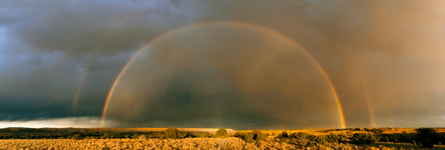 Stunning double rainbow arches over golden prairie landscape at sunset.
