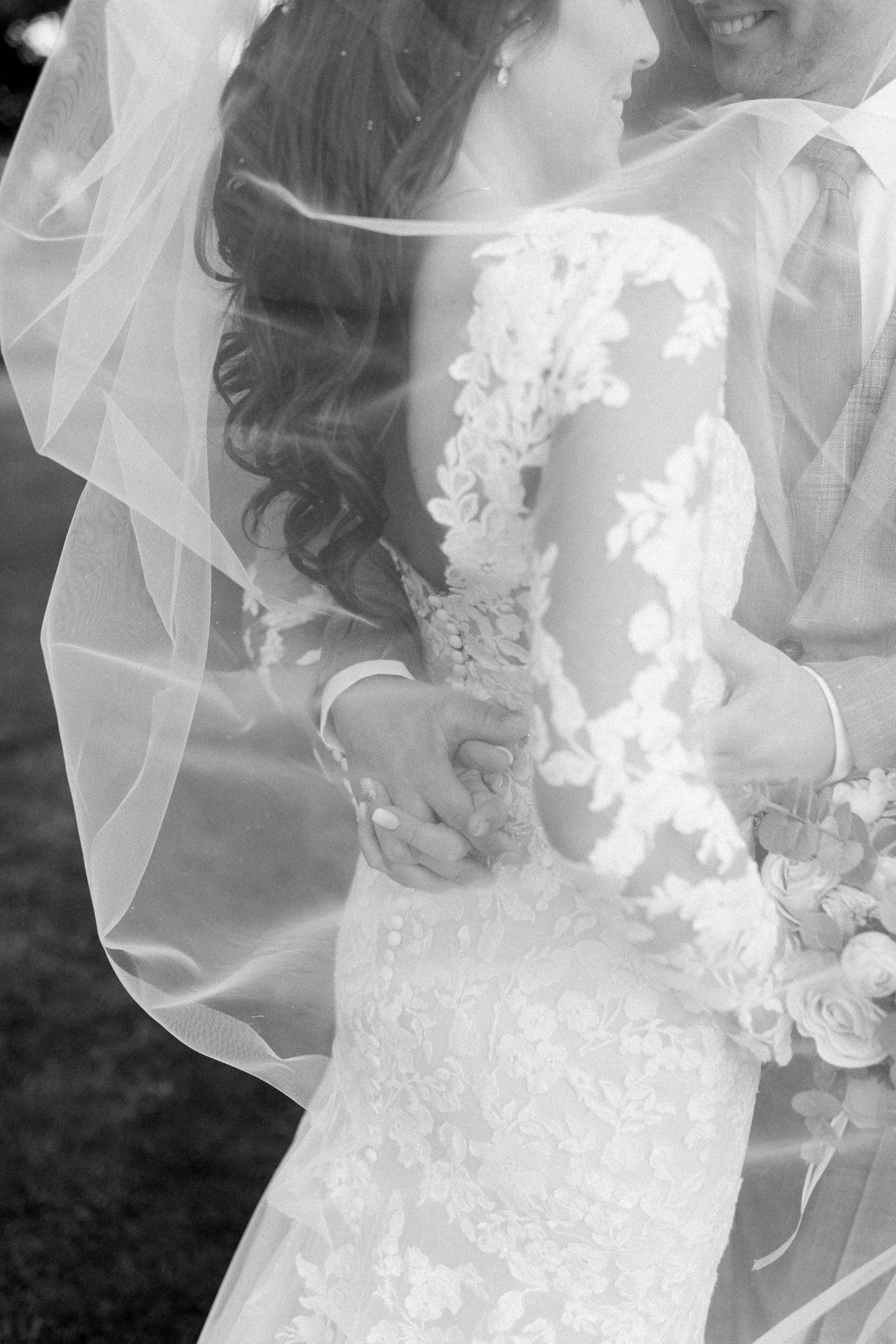 Elegant lace sleeve wedding dress with flowing veil shown in romantic black and white photography.