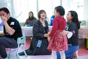 Adults and a child share a joyful moment at a colorful indoor event, with a woman laughing warmly.