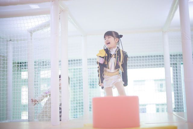 A cheerful young girl laughing and playing inside a bright indoor playground with white net walls.