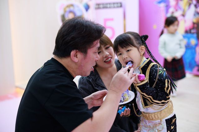 Adults feeding a young girl in a decorative outfit at a colorful birthday party celebration.
