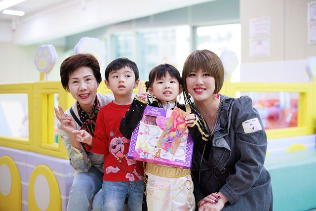 Two children and two women smile together at a colorful indoor play center, one child holding a gift bag.