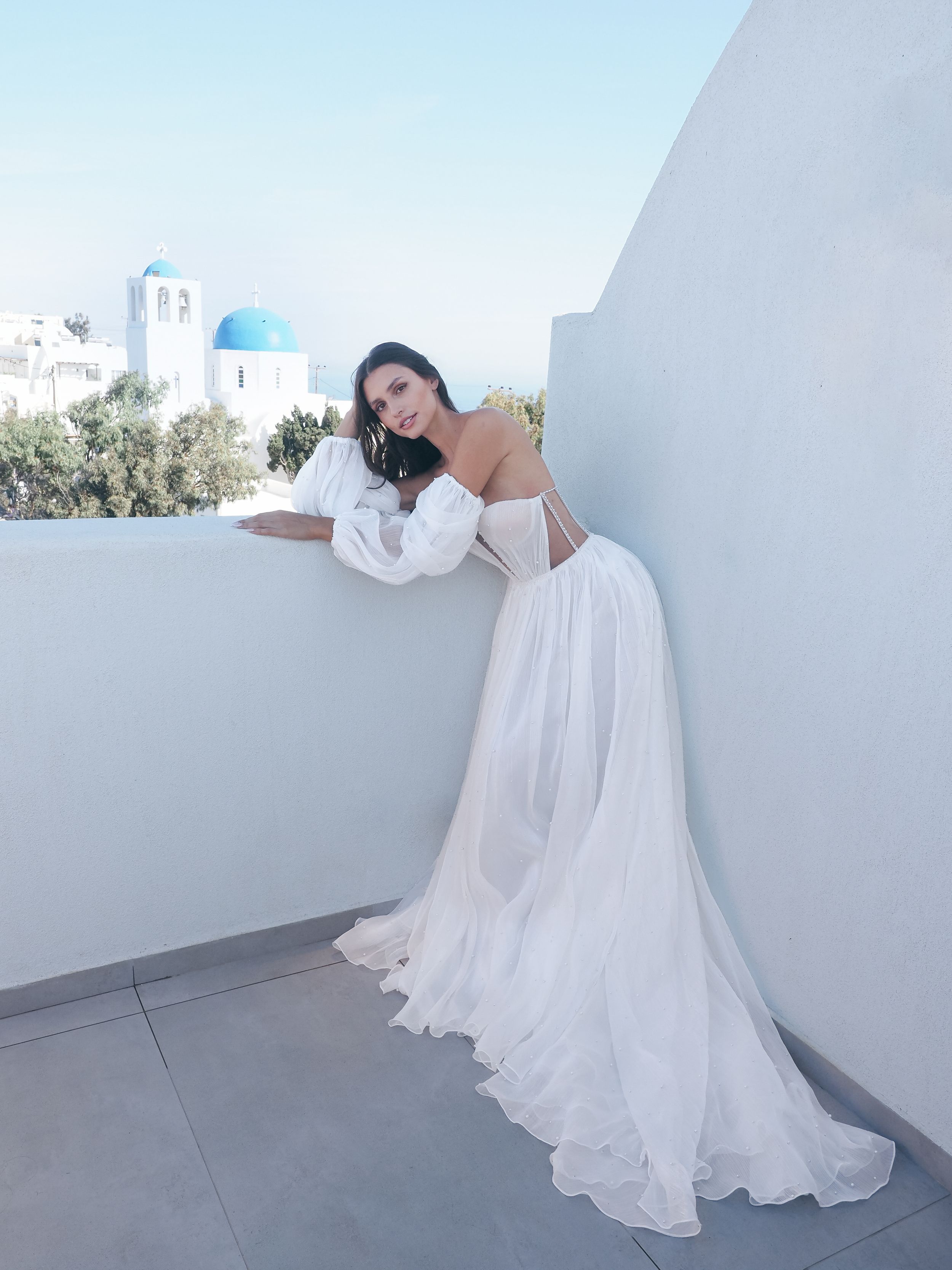 Elegant bridal photo with flowing white dress on a Santorini-style balcony.