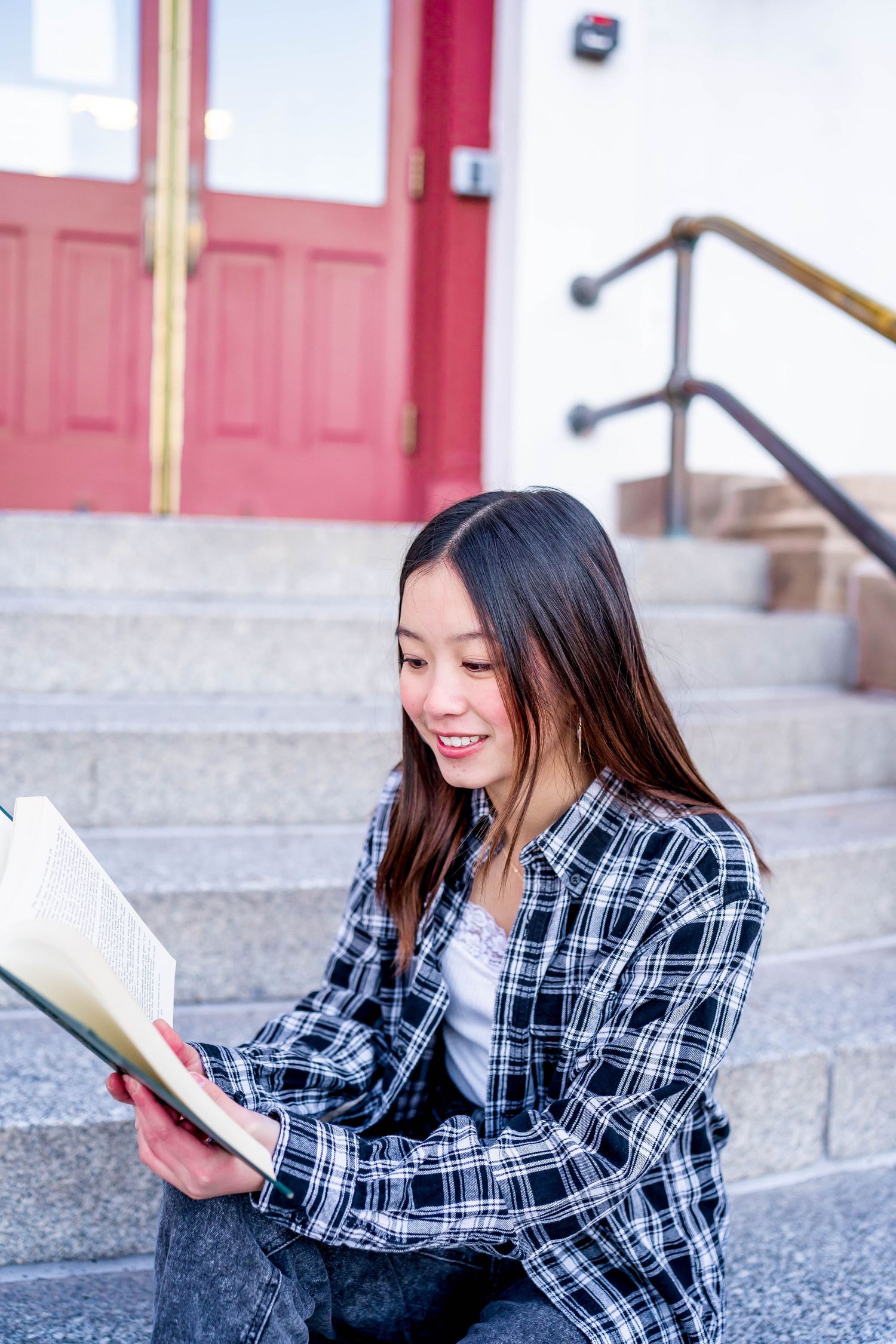 Student reading a book while sitting on concrete steps near a red door.