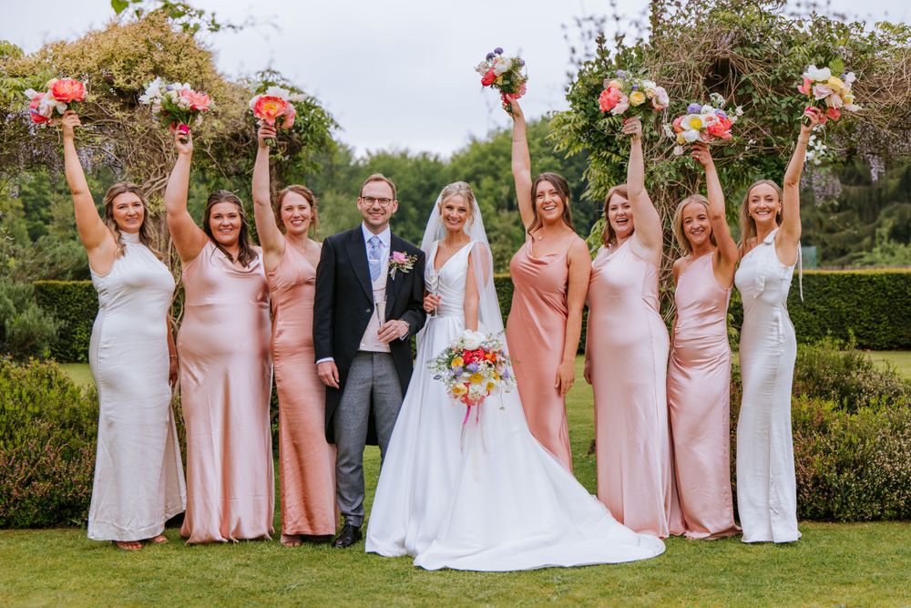 Bride and groom posing for a group photo with all the bridesmaids holding flowers high in the air in Cain Manor.