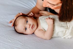 Nyfødtfotografering på Malmheim. Nyfødt gutt ligger på en seng og kikker i kamera mens mamma stryker han over hodet.