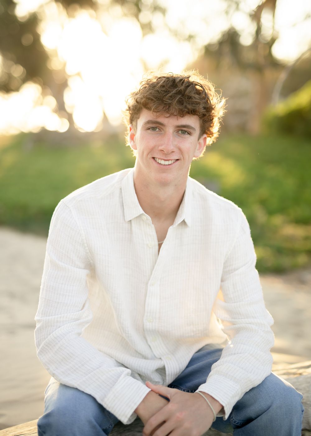 Person wearing a white sweater sits outdoors with a natural bokeh background during golden hour.