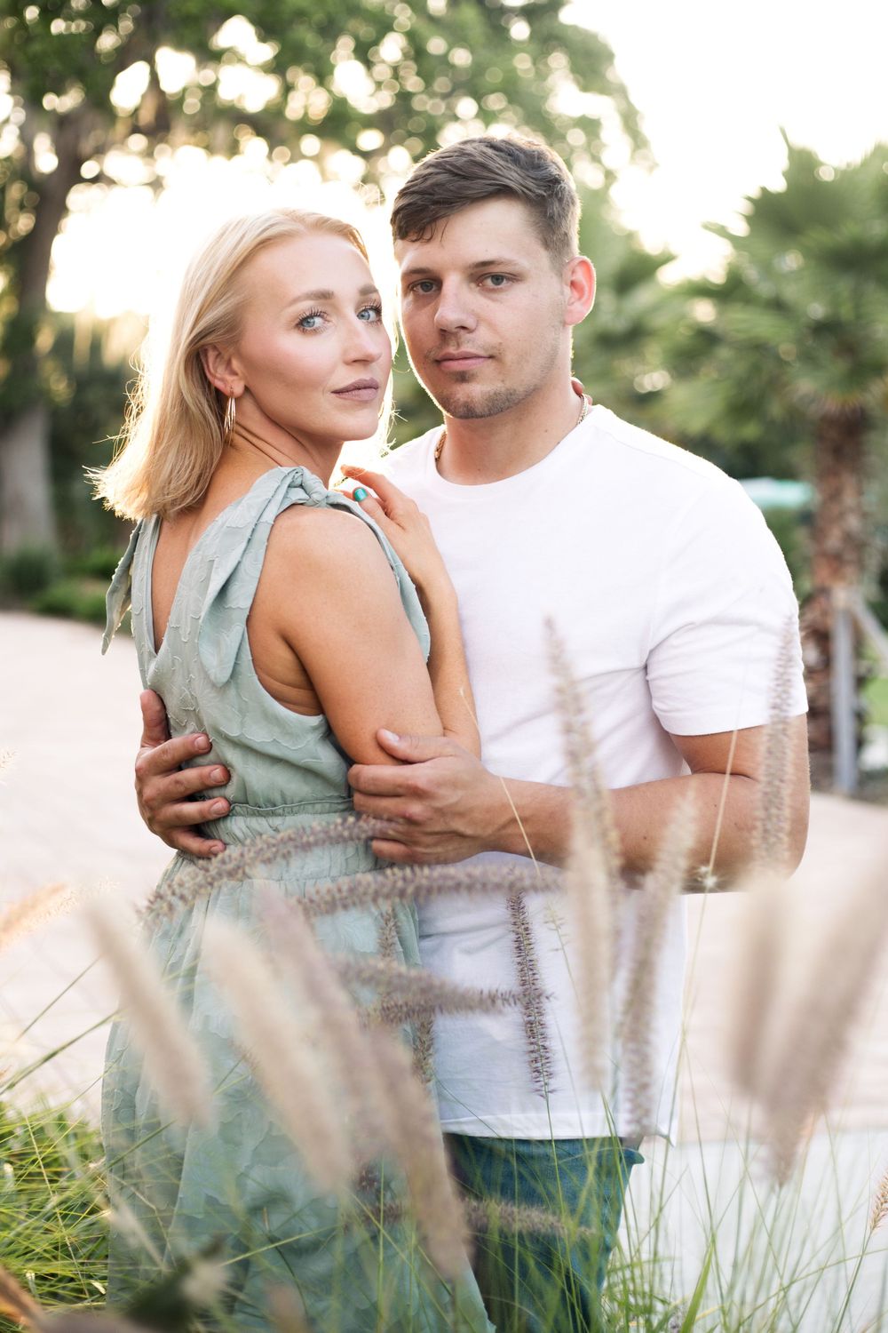 A couple poses together at sunset with ornamental grasses in the foreground.