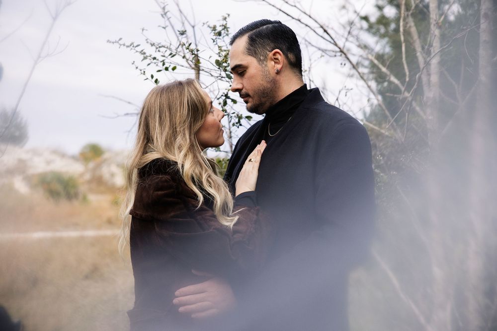 A romantic couple in dark winter clothing share an intimate moment together outdoors in misty natural scenery.