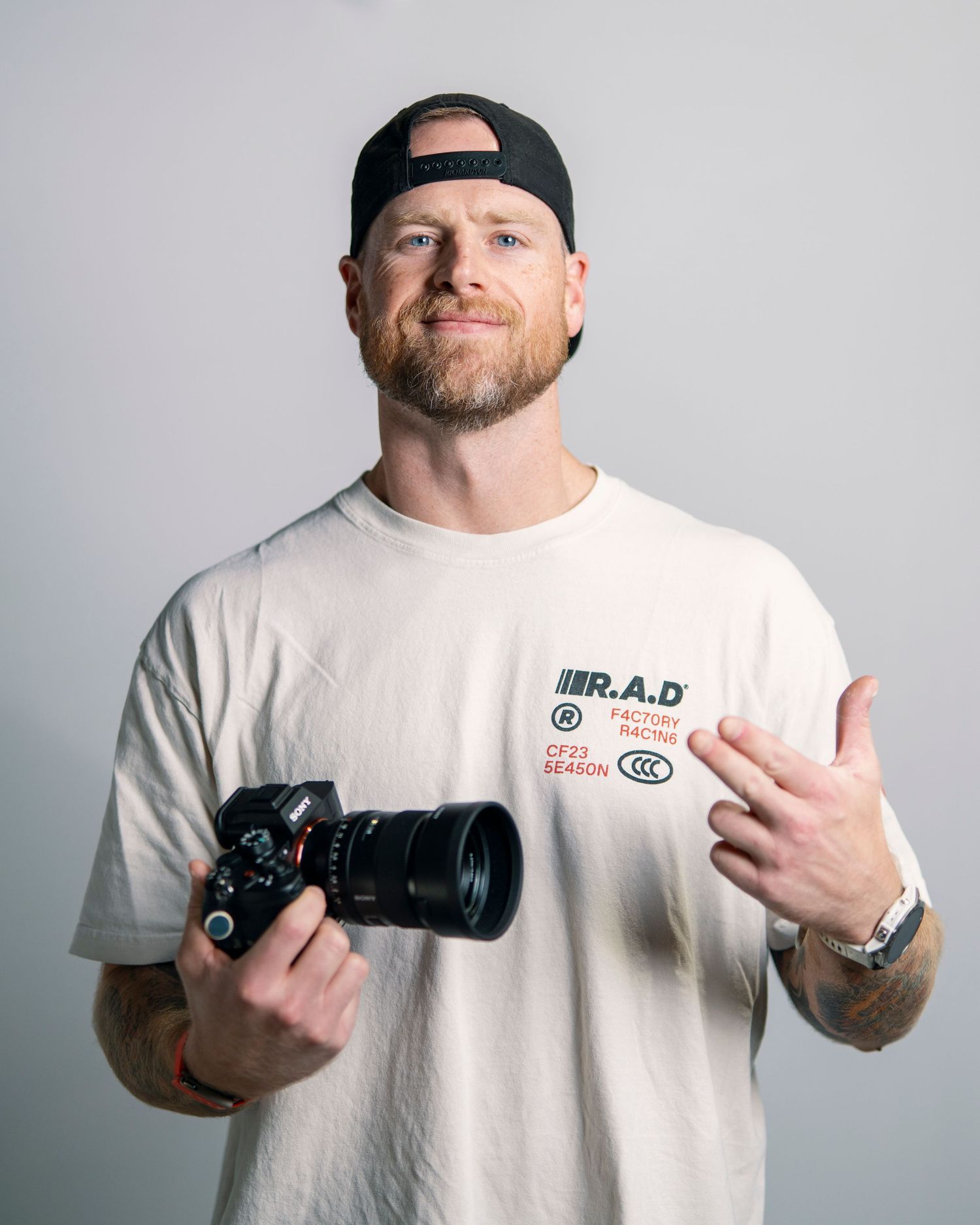 Professional photographer poses with camera equipment against white background.