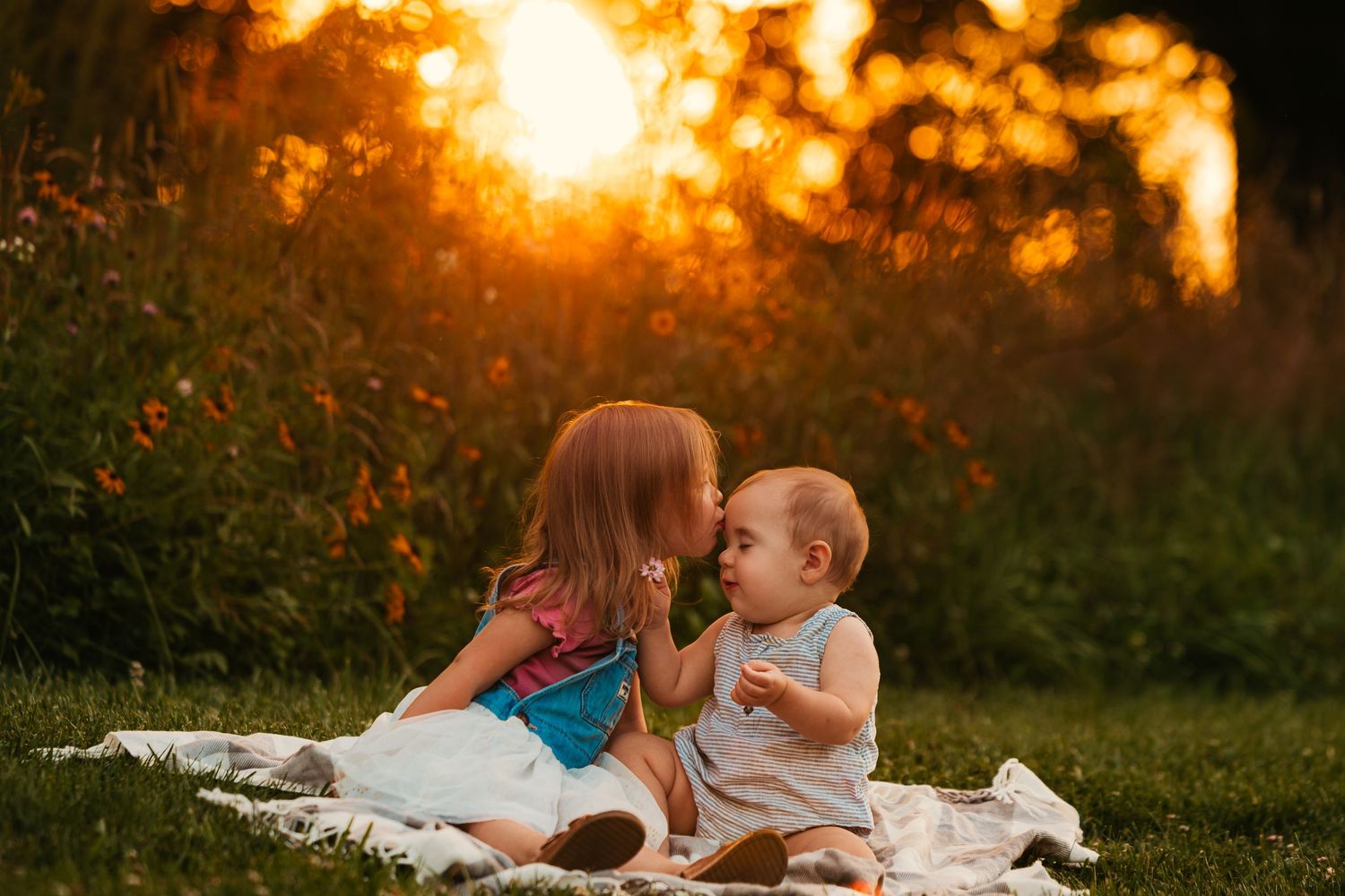 Couple lying on white blanket in grass during golden sunset in romantic outdoor setting.