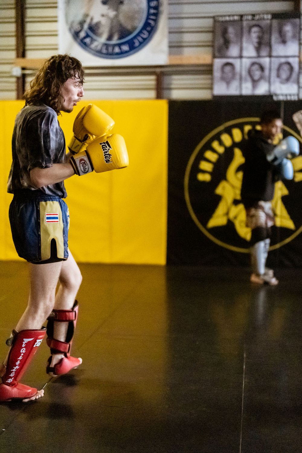 Boxer with yellow gloves practices stance in martial arts gym with samurai logo on wall.