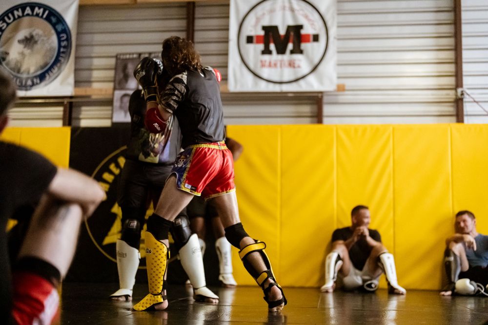 Martial arts sparring session in a gym with yellow walls and training equipment visible.