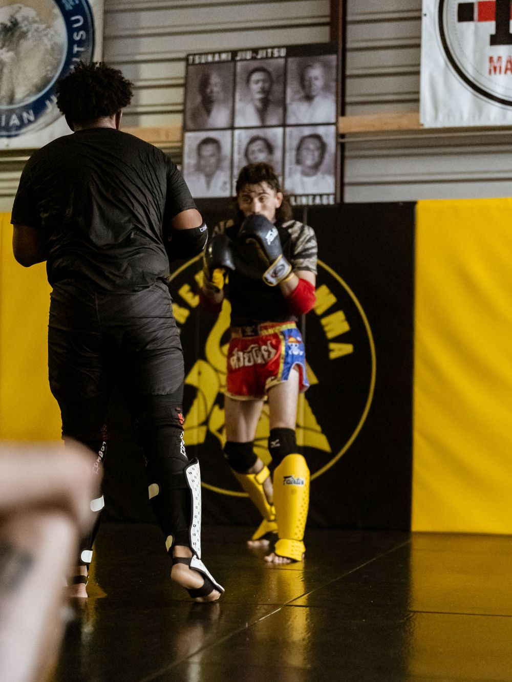 Combat sports training session taking place in front of a yellow wall with training posters.