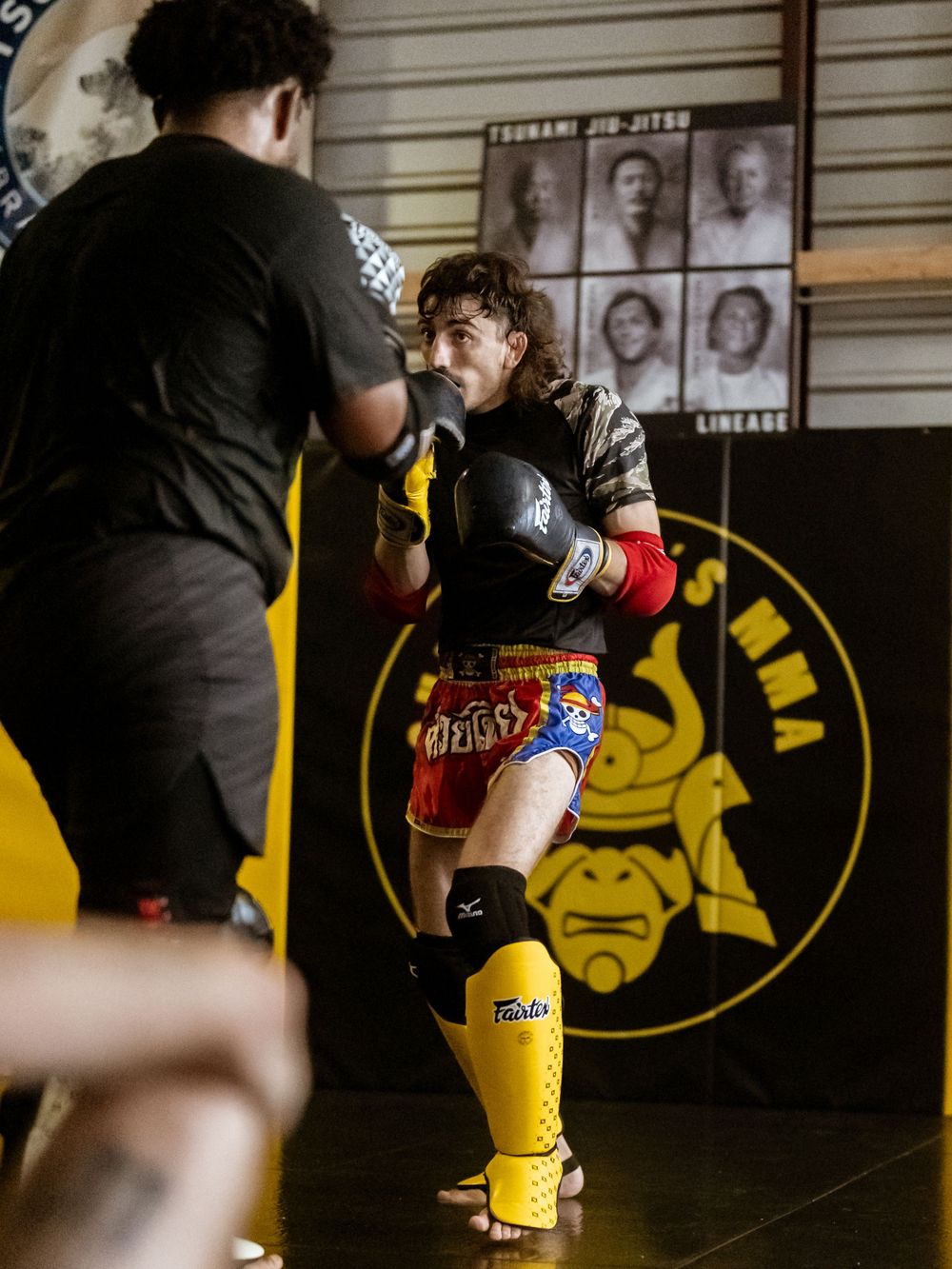 Kickboxing practice with protective gear in a martial arts gym with yellow padded walls.