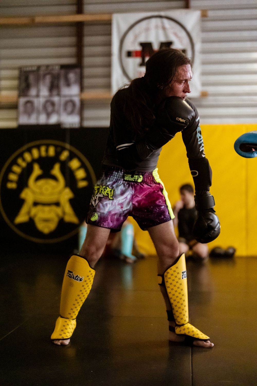 Fighter in colorful shorts and yellow boots takes fighting stance during training session.