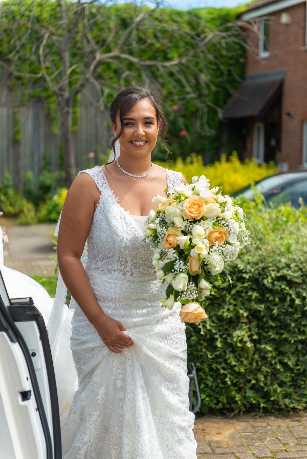 A wedding bouquet features peach and white flowers held against a white lace gown.