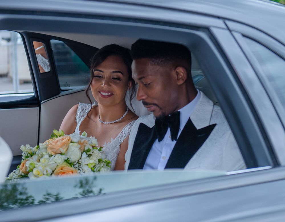 Newlyweds share a moment in the back seat of their wedding car with fresh bouquet.