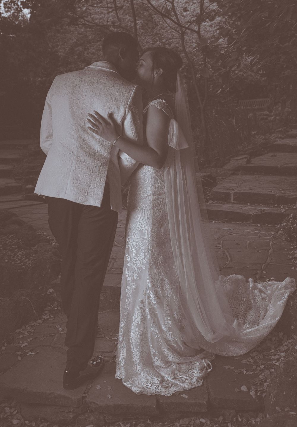 Romantic black and white portrait of couple embracing outdoors in wedding attire.