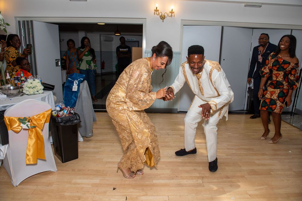 There first dance together in festive gold and white outfits at their reception celebration, with guests watching in the background.