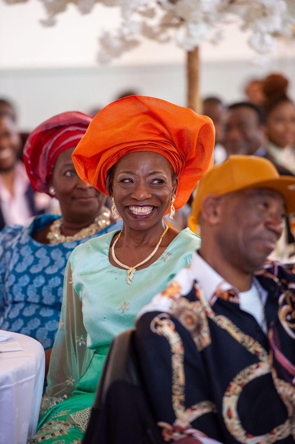 African celebration event with attendees wearing colorful traditional headwraps and formal attire at a festive gathering.