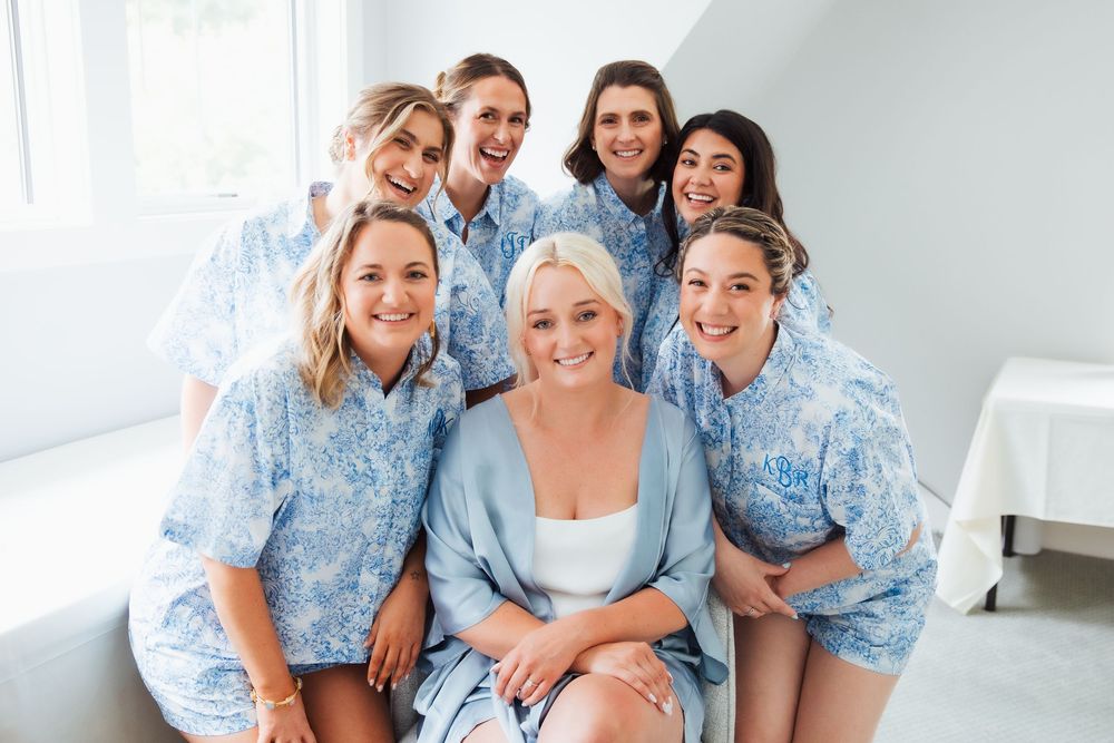 Bride and bridesmaids smiling together in matching blue floral robes during wedding morning preparations.