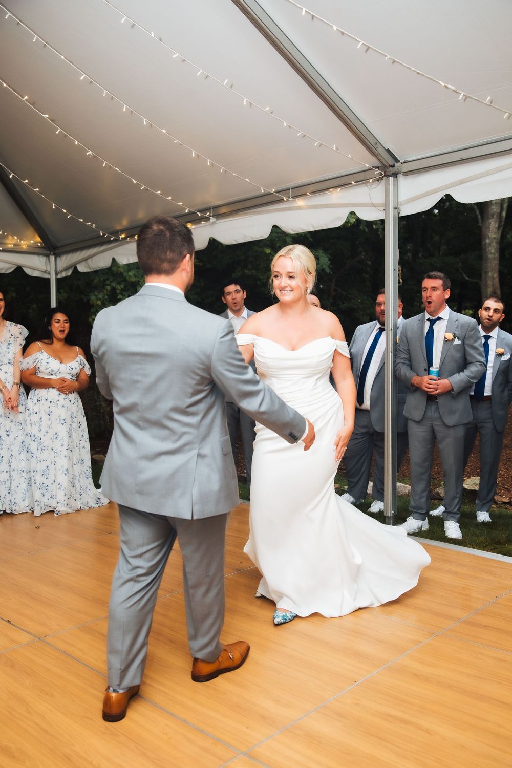 Bride and groom share their first dance under a white tent with string lights at an outdoor wedding reception.