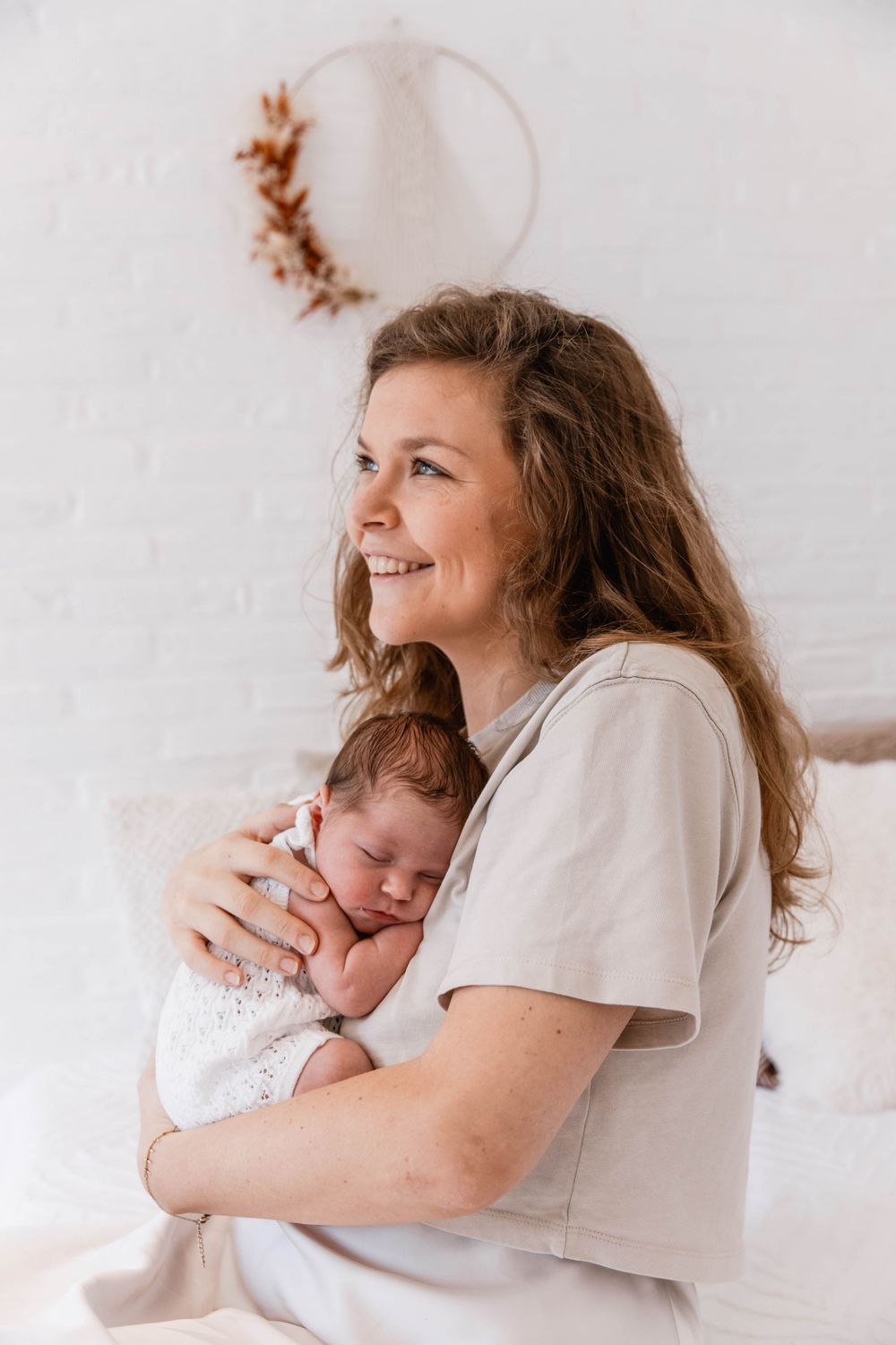 A tender moment between parent and newborn baby in casual white attire against a soft neutral background.