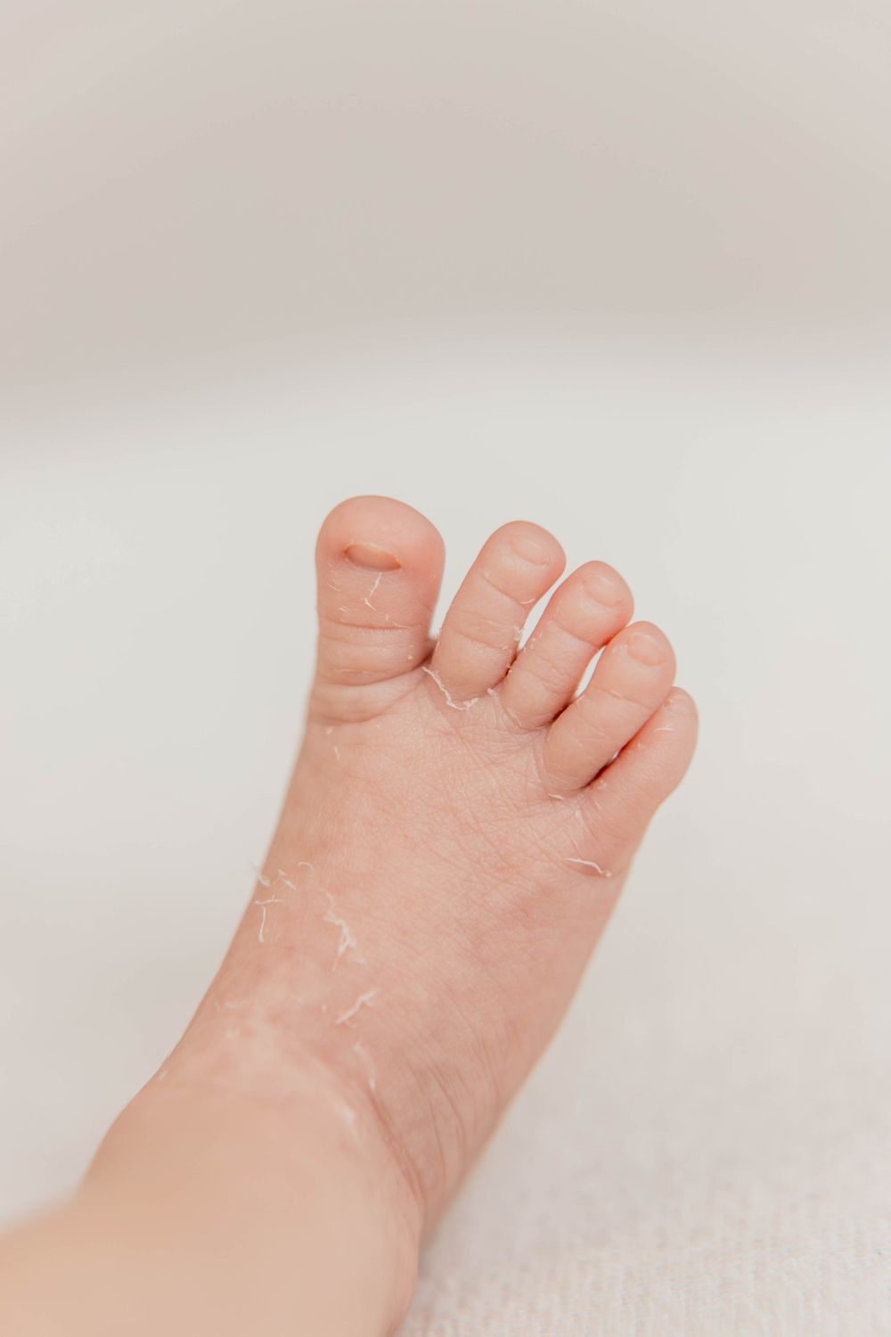 Close-up photo of a baby's tiny foot with delicate toes against a light background.