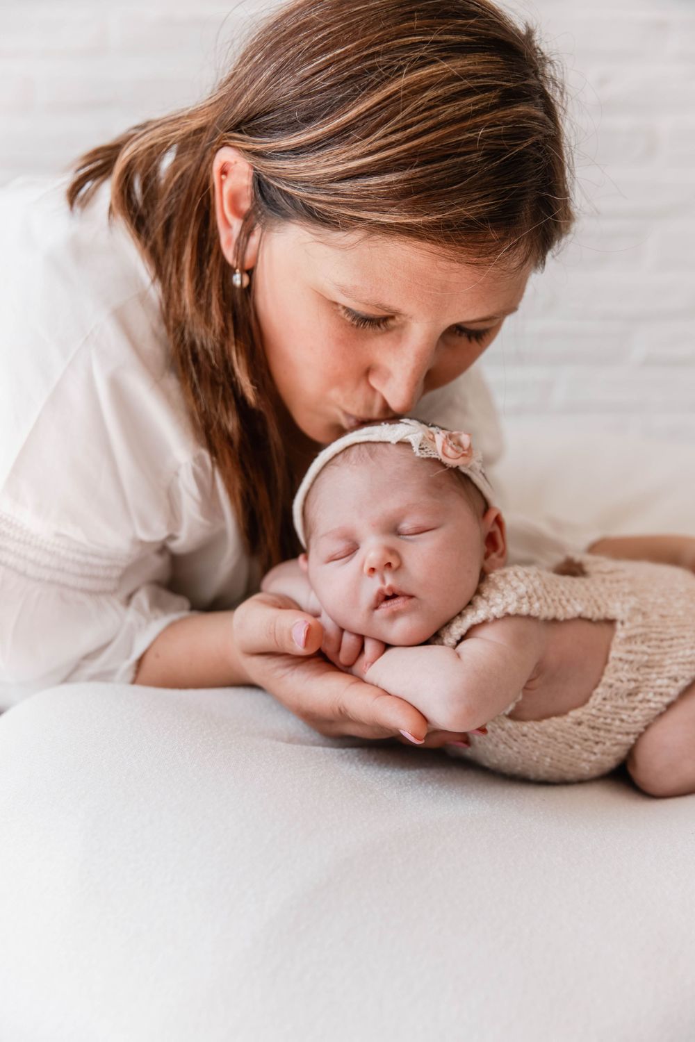 A tender moment between parent and newborn as they rest together on white bedding.